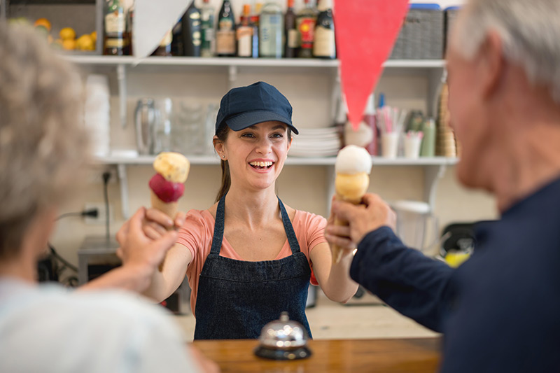 female ice cream shop worker serving cones to customers