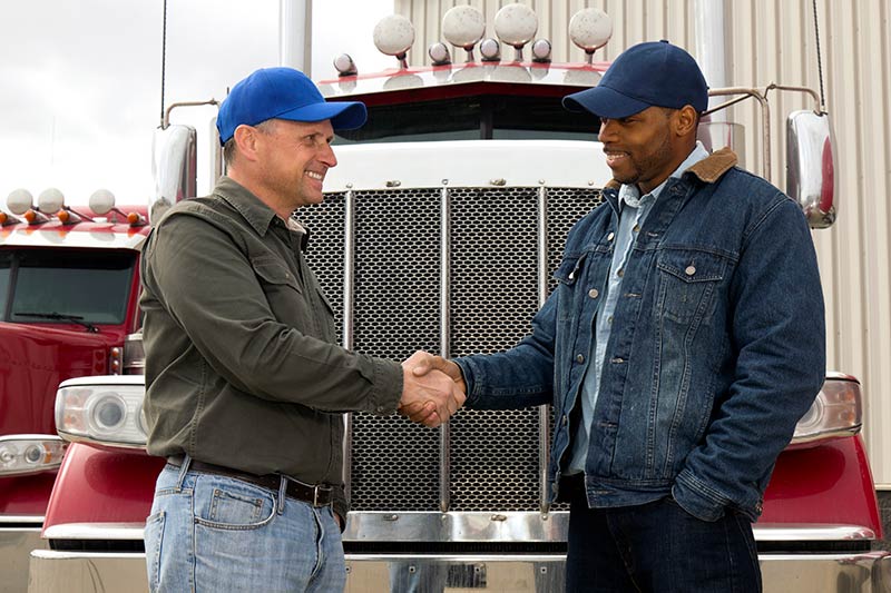 two male truck drivers shaking hands in front of a semi truck