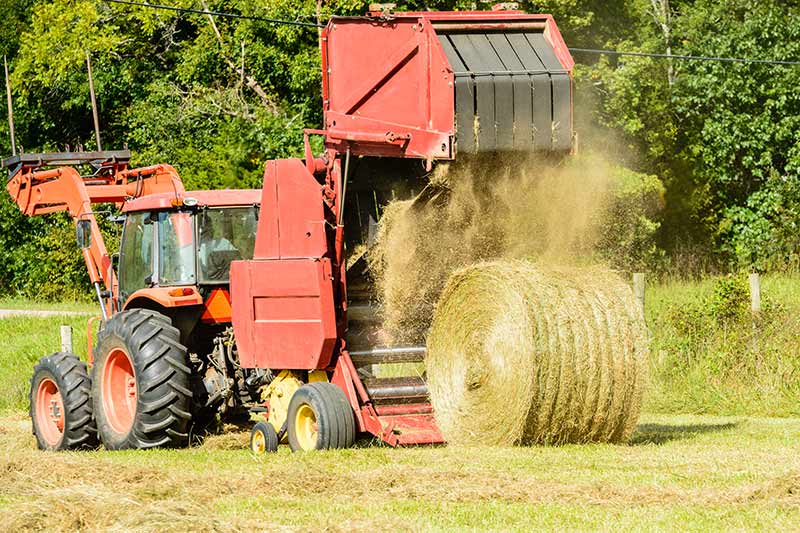 large red hay baler making a large round hay bale on a farm