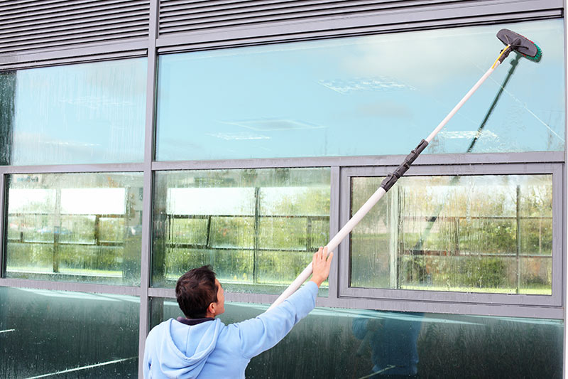 professional window cleaner scrubbing a window using an extension pole
