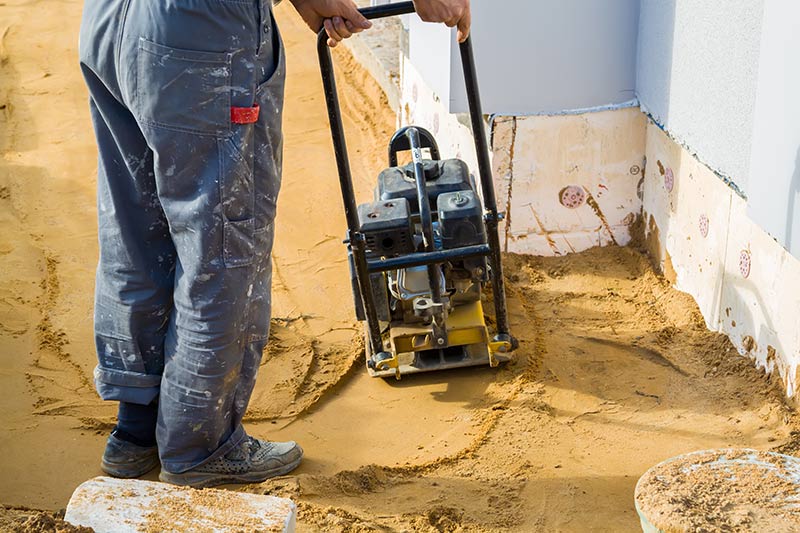 worker operating a plate compactor in a small area