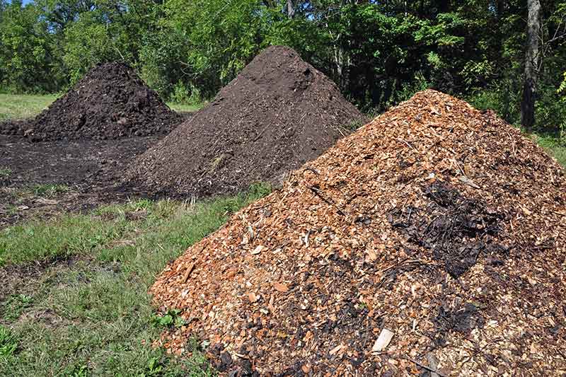 three large piles of mulch in a large yard