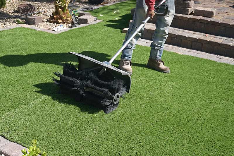 worker rolling artificial grass with a rolling brush