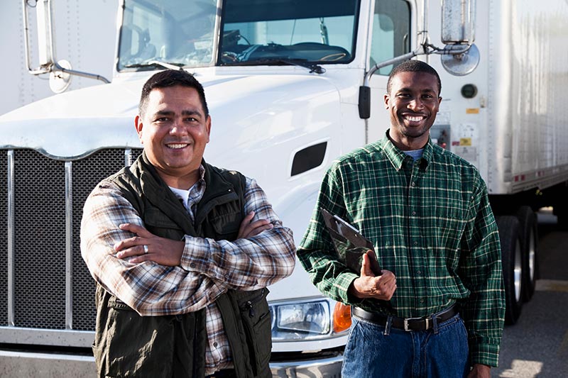 two smiling commercial truck drivers near their trucks